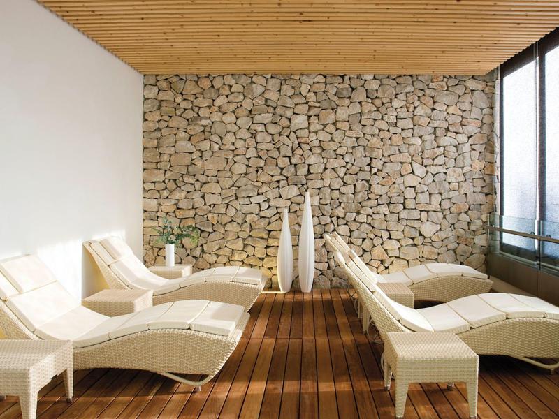 Area lounge rilassante con poltrone crema, muro in pietra, pavimento in legno e grandi finestre