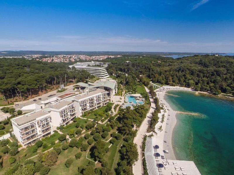 Vista aerea di un hotel con piscina e spiaggia, circondato da foresta e acqua limpida.