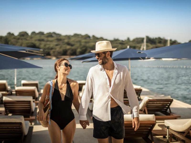 Coppia in costume da bagno che cammina sulla spiaggia con lettini e ombrelloni vicino all'acqua.