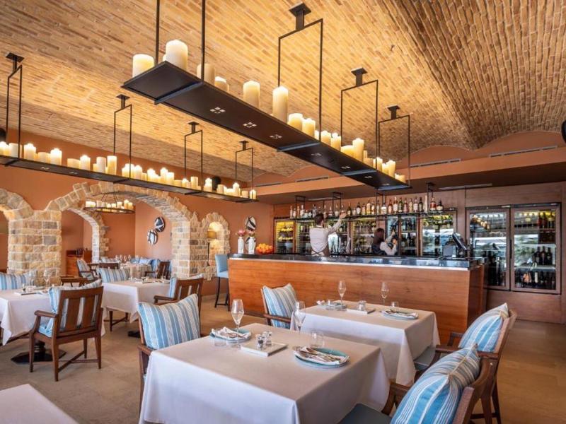 Ristorante elegante con tovaglie bianche, archi in pietra rustici e un bar sullo sfondo.