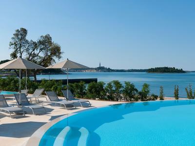 Pool mit Liegestühlen und Sonnenschirmen, Meerblick und klarem Himmel im Hintergrund.