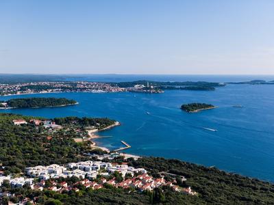 Blick auf eine Küstenstadt mit klarem blauem Wasser und bewaldeten Hügeln im Vordergrund.
