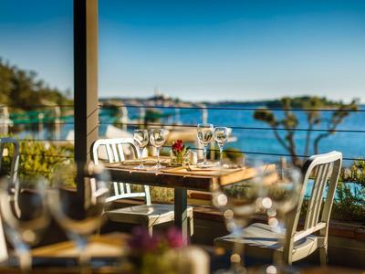 Terrasse eines Hotels mit Holztisch und weißen Stühlen mit Blick auf Meer und blauen Himmel.