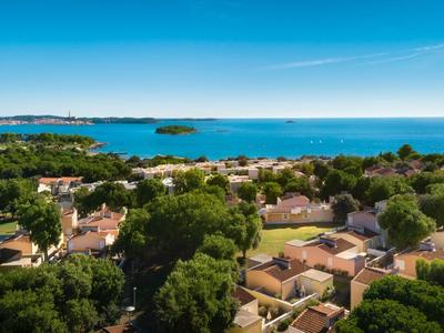 Blick auf eine Küstenstadt mit Häusern, Bäumen und blauem Meer unter klarem Himmel.