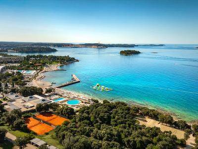 Küstenlandschaft mit klarem blauem Meer, Sandstrand und grünen Bäumen neben einem Hotel.