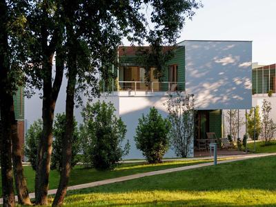 Modern wit vakantiehuis met grote glazen gevel, omgeven door bomen en groen gras.
