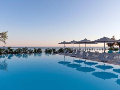 Piscina infinity con ombrelloni e vista sul mare sotto un cielo limpido.