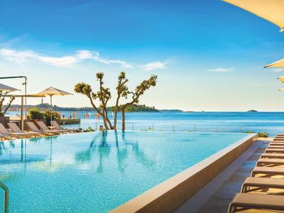 Modern zwembad met ligbedden en parasols naast zee en blauwe lucht.