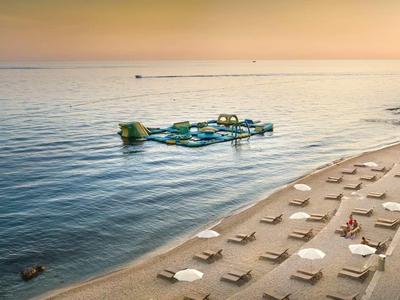 Zonsondergang op het strand met ligstoelen en een boot op het water.