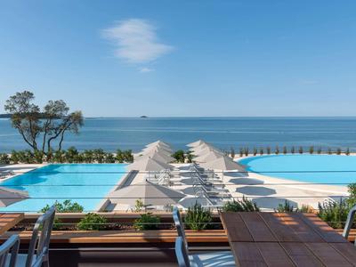 Infinity zwembad met ligstoelen en zeezicht onder een heldere lucht