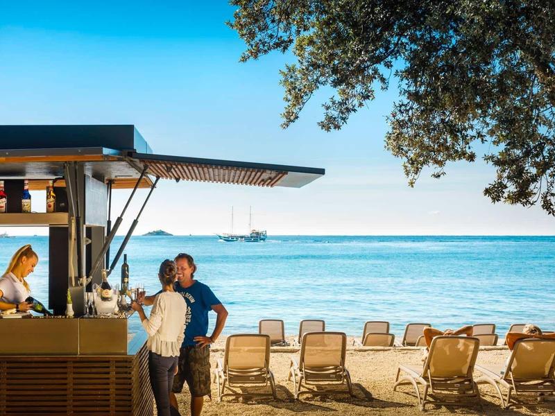 Bar na plaży z klientami obok leżaków nad morzem pod niebieskim niebem