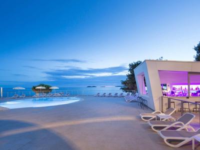 Nowoczesny basen na zewnątrz z leżakami i barem o fioletowym świetle o zmierzchu.