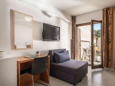 Helles Hotelzimmer mit Sofa, Schreibtisch, Fernseher und Balkon mit Blick auf Berge.