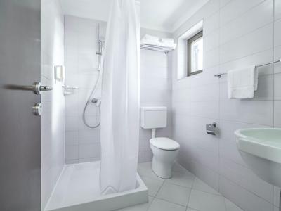 Kleines, weiß gekacheltes Badezimmer mit Dusche, WC und Handtüchern.
