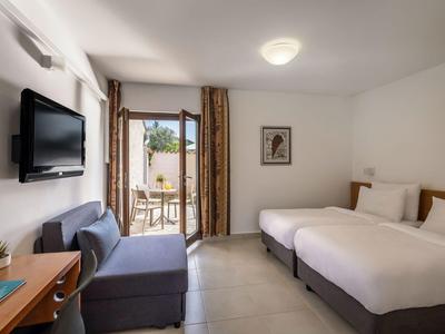Hotelzimmer mit zwei Einzelbetten, Sofa, Fernseher und Zugang zu Balkon mit Außenmöbeln.