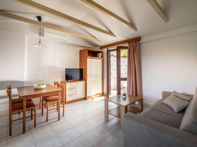 Helles Wohn- und Esszimmer mit Holzmöbeln, Sofa und Zugang zu Balkon mit Vorhängen.