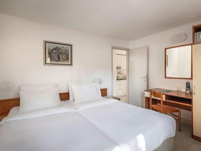 Hell eingerichtetes Hotelzimmer mit zwei Betten, Nachttischen und Schrank mit Spiegel.