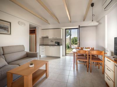 Helles Wohnzimmer mit grauem Sofa, Holztisch, Essbereich und kleiner Küchenzeile mit Blick nach draußen.