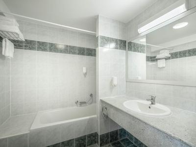 Helles Hotelbadezimmer mit Badewanne, großem Spiegel und Waschbecken mit weißem Marmorplatten.