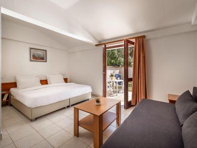 Helles Hotelzimmer mit zwei Einzelbetten, Sofa, Holztisch und Terrasse mit Blick ins Grüne.