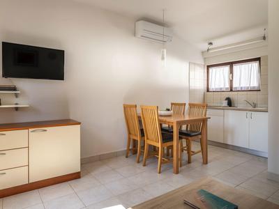 Kleiner Essbereich mit Holztisch und Stühlen neben einer weißen Küchenzeile und Fernseher an der Wand.