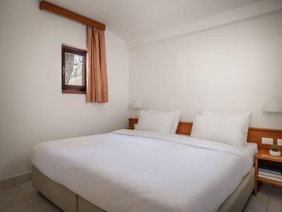 Ein einfaches Hotelzimmer mit einem großen Bett, weißen Wänden und kleinem Fenster mit Vorhang.