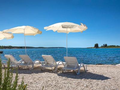 Leżaki i parasole na żwirowej plaży z widokiem na niebieskie morze i wyspę.