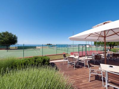 Taras z stołami i parasolami z widokiem na kort tenisowy i morze pod błękitnym niebem