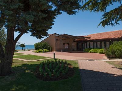 Budynek hotelu z czerwonym dachem otoczony drzewami z widokiem na morze pod słonecznym niebem