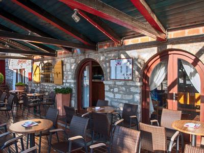 Przytulny zewnętrzny taras kawiarni z stołami i krzesłami pod drewnianym i szklanym dachem.