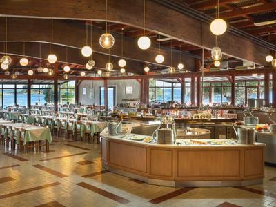 Duża jadalnia z stołami, krzesłami i centralnym stanowiskiem obsługi pod ciepłym oświetleniem sufitowym.