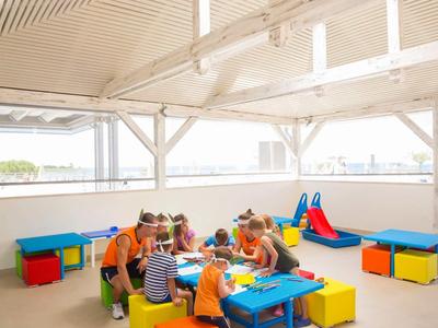 Dzieci bawią się w pomieszczeniu przy kolorowych stolikach z zabawkami w jasnym pokoju.