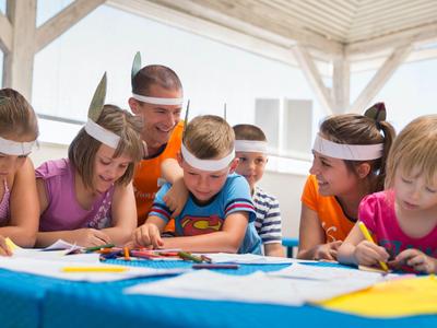 Kinder mit Partyhüten sitzen an einem Tisch und malen auf Papier, umgeben von Spaß und Kreativität.