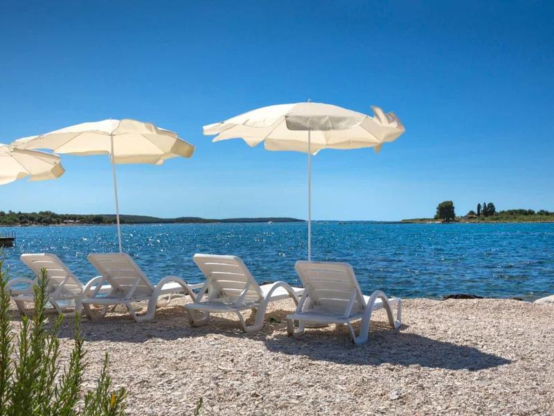 Trzy leżaki z białymi parasolami na kamienistej plaży z widokiem na morze.