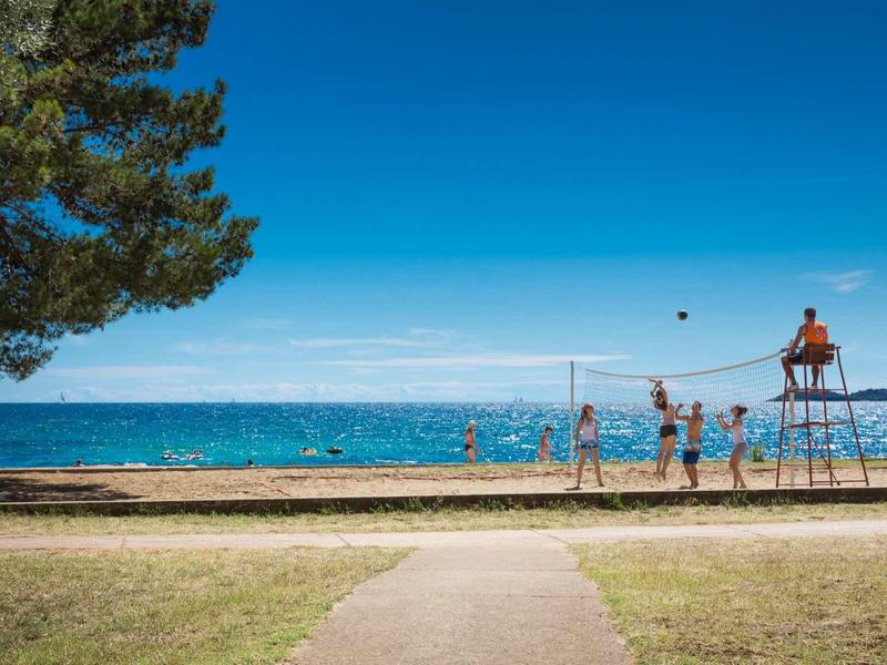 Plaża z siatką do siatkówki, wieżą ratownika i ludźmi przy brzegu pod czystym niebem.