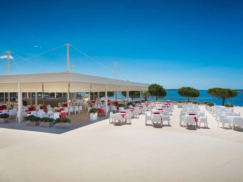 Restauracja na świeżym powietrzu z miejscami do siedzenia na zewnątrz i widokiem na niebieskie morze pod przejrzystym niebem.