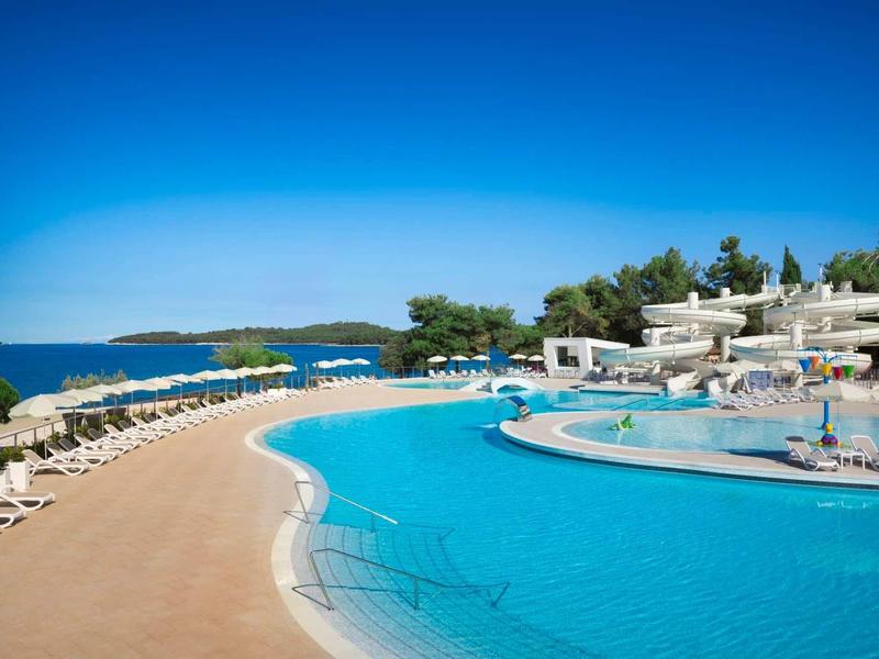 Duży basen z leżakami i widokiem na morze w ośrodku hotelowym.