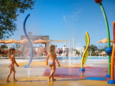 Kinderen spelen en lopen op een kleurrijke waterspeeltuin buiten in de zon.