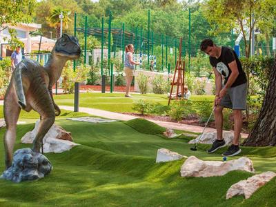 Osoba hrající minigolf na zeleném hřišti s figurkou dinosaura.