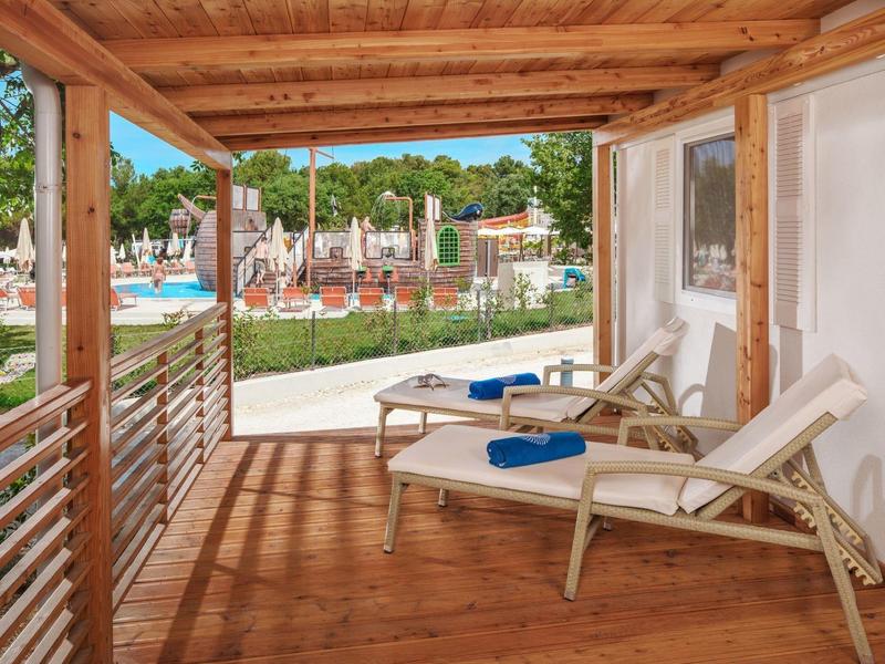 Overdekt terras met twee ligstoelen met uitzicht op de tuin en het zwembad.