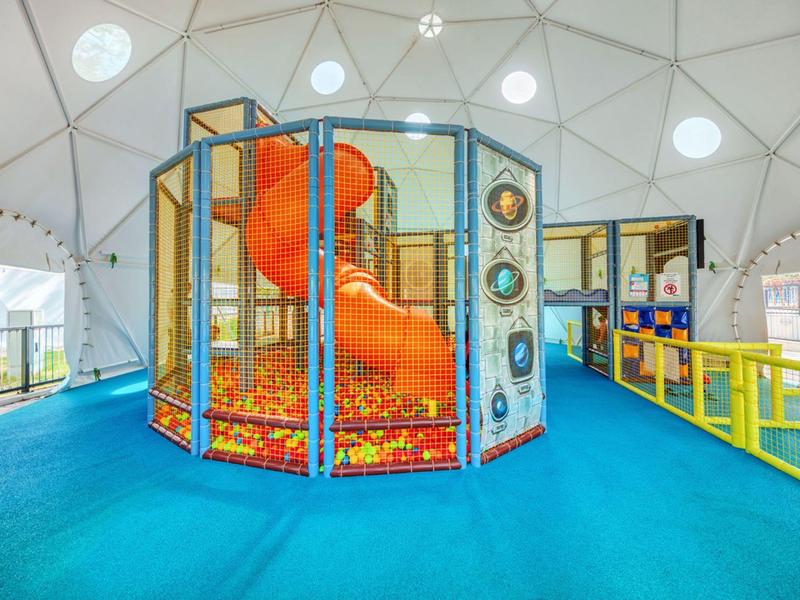 Kleurrijke speeltuin voor kinderen met glijbaan en ballenbak in koepelstructuur.