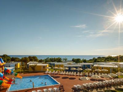 Piscina del hotel con tumbonas y vista al mar bajo cielo despejado, día soleado.