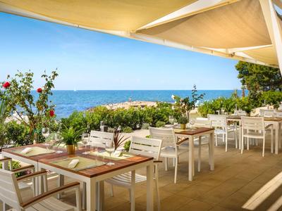 Terrazza di ristorante con tavoli e sedie bianchi che si affaccia sul mare sotto un cielo sereno.