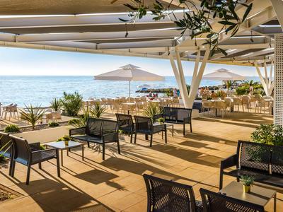 Terrazza coperta con sedie e tavoli accanto a una spiaggia con vista sul mare.