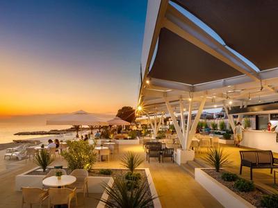 Strandpromenade bei Sonnenuntergang mit Tischen, Stühlen und moderner Beleuchtung.