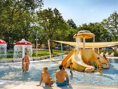 Niños juegan en un área de agua poco profunda con toboganes y juegos de agua al aire libre.