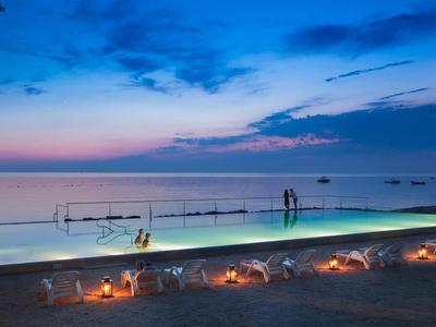 Piscina a sfioro con illuminazione e vista sul mare al tramonto.