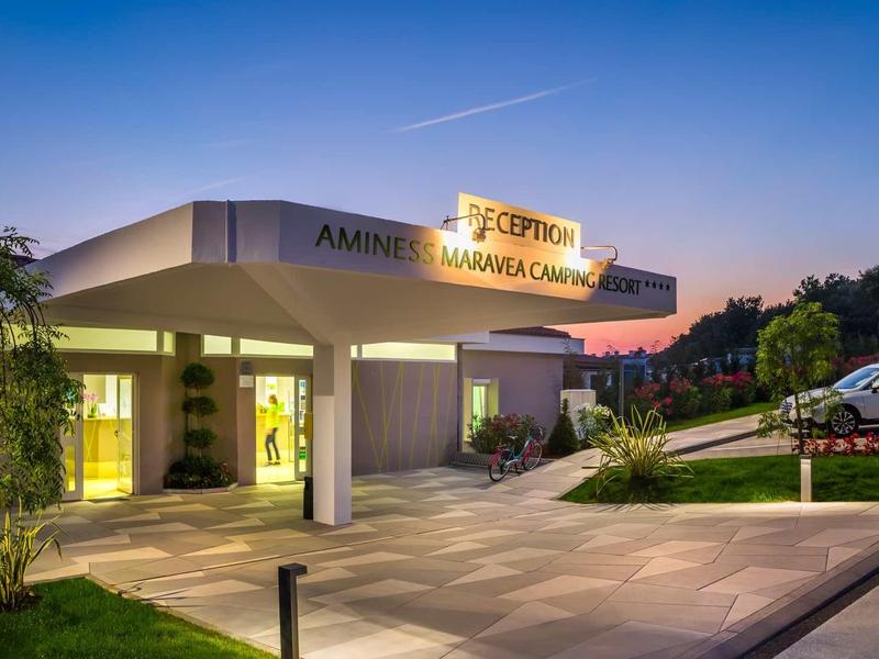 Entrada de hotel moderna con cartel iluminado al atardecer y coches aparcados.