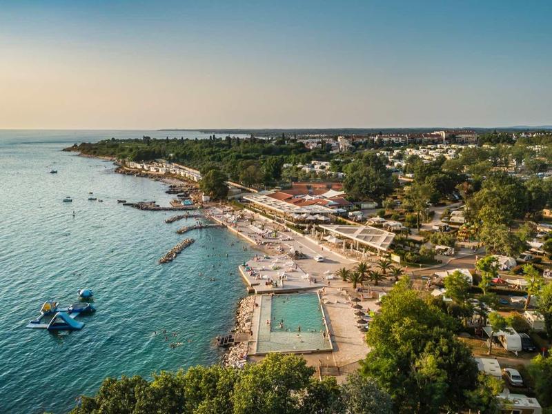 Vista aérea de una costa con piscinas y áreas de descanso junto al mar bajo un cielo despejado.