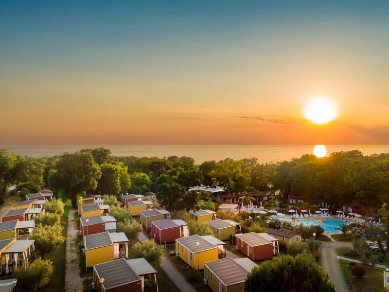 Camping con muchas caravanas al atardecer junto al mar con cielo despejado.